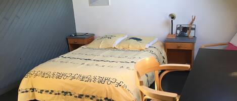 A bedroom with a bed, a chair, a desk, and a nightstand.