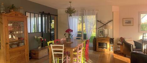 A cozy living room with a wooden dining table, colorful chairs, a fireplace, and a cabinet with glass doors.