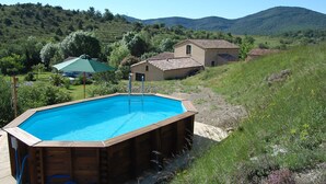 Une piscine extérieure dotée d’une terrasse en bois, entourée d’un paysage verdoyant et luxuriant, avec des collines en arrière-plan.