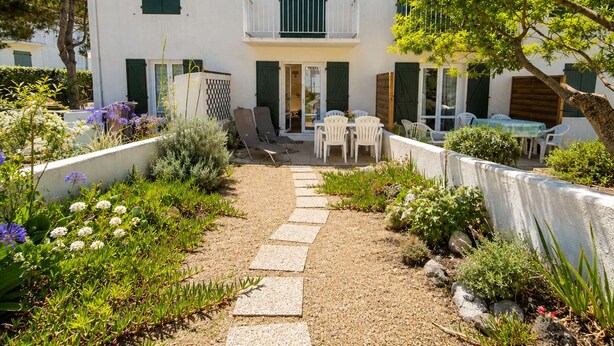 A two-story building with a balcony, a garden with a gravel path, and outdoor seating.