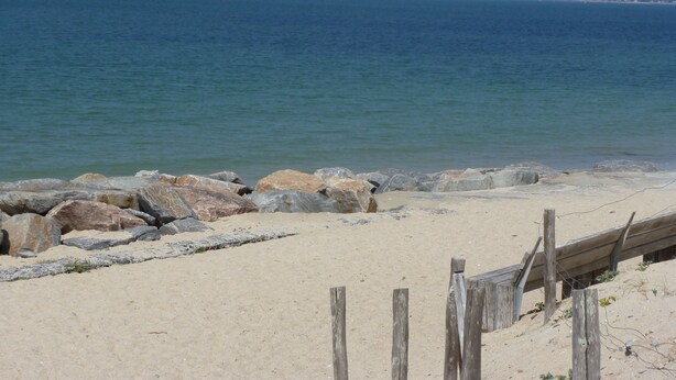 Ein Strand mit einer Holzzaun und großen Felsen im Vordergrund.