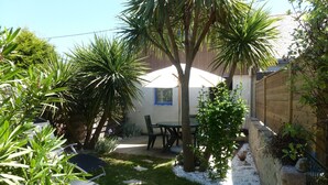 Ein Patio mit Tisch und Stühlen, umgeben von Pflanzen und einem Holzzaun.