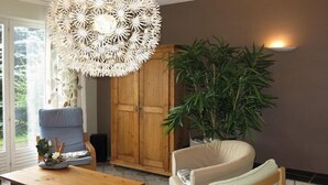 A room with a wooden cabinet, a blue chair, a beige sofa, a wooden coffee table, and a large potted plant. - Spacious 3-star house in the Vosges (Nayemont-Les-Fosses)