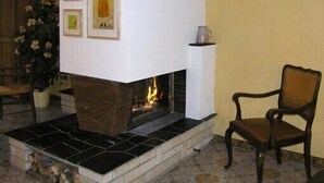 A fireplace with a mantel, a chair, and framed pictures on the wall. - Spacious 3-star house in the Vosges (Nayemont-Les-Fosses)
