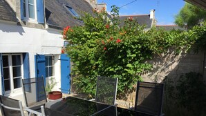 Ein Gartenbereich mit einem Glastisch und Stühlen, einer blauen Tür und einem Baum mit roten Blüten.