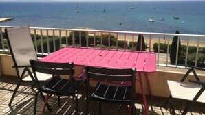 A balcony with a table and chairs overlooking the sea.