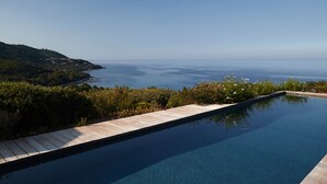 A clear view of a swimming pool with a wooden deck, surrounded by greenery and overlooking a body of water.