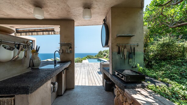 An outdoor kitchen with a view of the ocean, a wooden deck, and a stone wall.