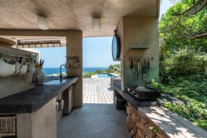 An outdoor kitchen with a view of the ocean, a wooden deck, and a stone wall. - Facing the sea, air-conditioned villa for 10 people, with spa and secure heated pool (Conca)