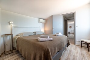A bedroom with a large bed, a bedside table, an air conditioning unit, and a door leading to another room. - Facing the sea, air-conditioned villa for 10 people, with spa and secure heated pool (Conca)