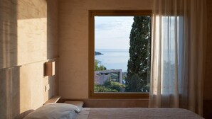 A bedroom with a large window, a bed, a bedside table, and a wall-mounted light fixture.