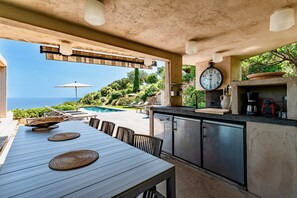 An outdoor dining area with a view of the sea, a pool, and a stone wall. - Facing the sea, air-conditioned villa for 10 people, with spa and secure heated pool (Conca)