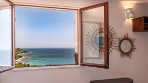 A room with a large window overlooking a coastal view, a wooden cabinet, and two wall-mounted decorative items.