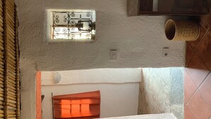 Una habitación de diseño rústico, con una ventana de rejas de hierro decorativas, una pequeña mesa de madera, una cesta de mimbre y suelo de baldosas.