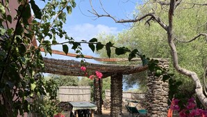 Ein Steinweg führt zu einer hölzernen Pergola, darunter befinden sich ein Tisch und Stühle.