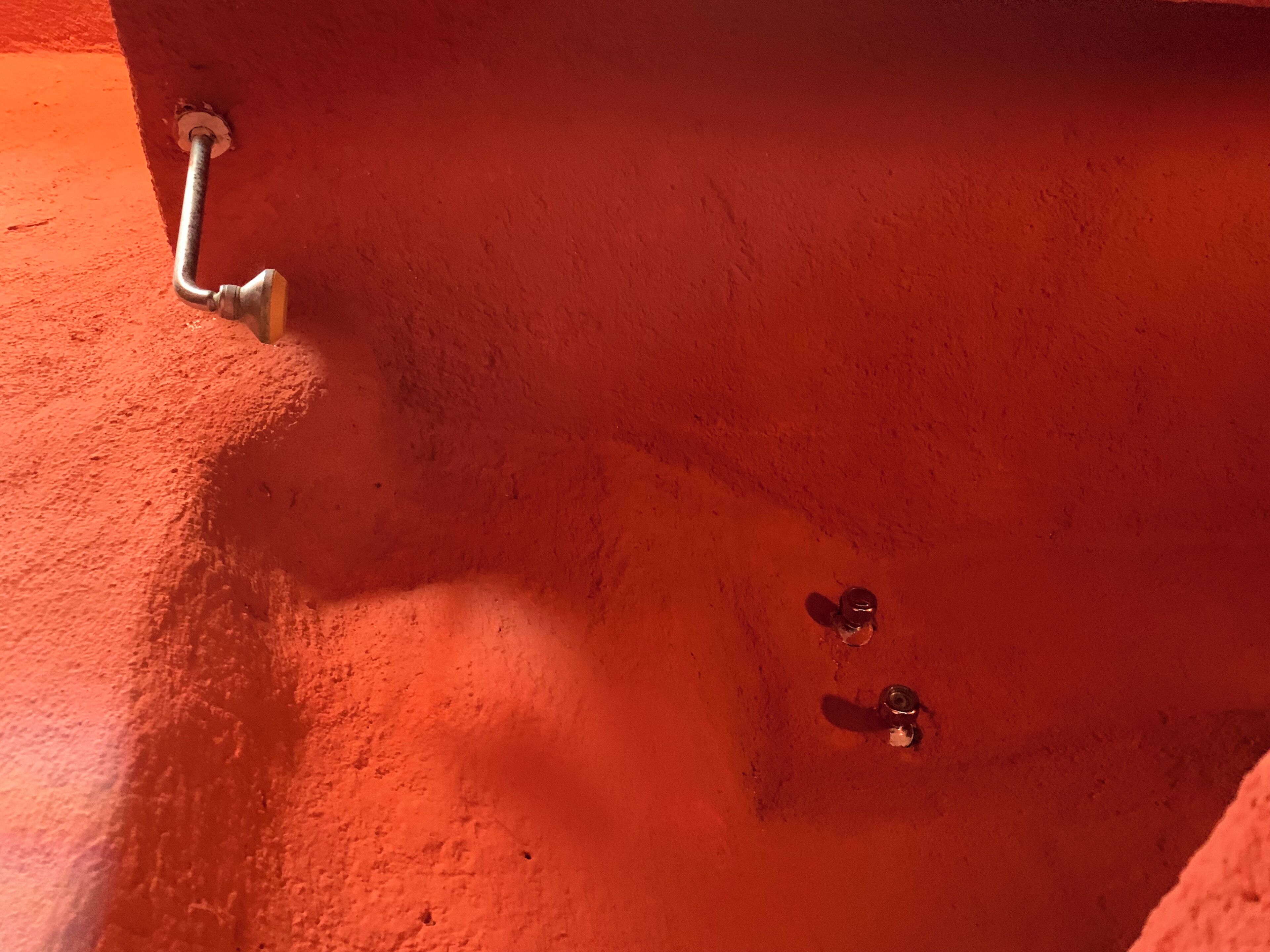 Een rode muur met een metalen bevestiging, mogelijk een lichtschakelaar of een onderdeel van de sanitaire installatie.