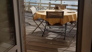 Un área de comedor al aire libre con una mesa y sillas bajo un toldo a rayas, con vistas a un puerto deportivo con barcos.