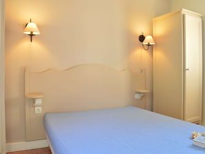 A bedroom with a bed, two wall-mounted lamps, and a wardrobe.