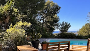 Eine Holzterrasse mit Gartenmöbeln, einem Swimmingpool und Blick auf das Meer.