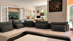 Ein modernes Wohnzimmer mit einem Ecksofa, einem Flachbildfernseher und einer Essecke mit Tisch und Stühlen.