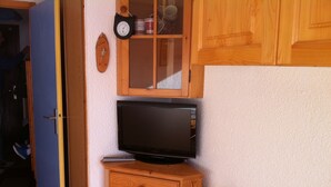 A room with a wooden cabinet, a television on top, and a small shelf with decorative items. - Les Saisies, Available January and March, 4 people, resort center (Hauteluce)