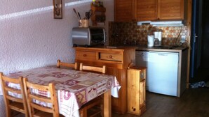 A compact kitchen with wooden cabinets, a small refrigerator, and a table with chairs. - Les Saisies, Available January and March, 4 people, resort center (Hauteluce)