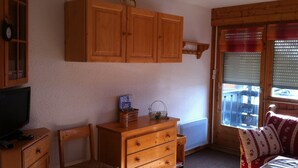 A room with wooden furniture, including a dresser, a chair, and a cabinet. There is a window with blinds and a view outside. - Les Saisies, Available January and March, 4 people, resort center (Hauteluce)