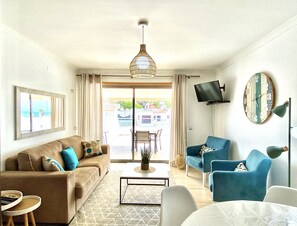 A living room with a sofa, armchairs, a coffee table, a TV, and a clock on the wall.