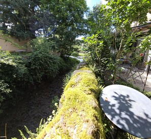 A garden with a moss-covered wall, a metal table, and a bench. - Au Bord de la Rivière, Charming gîte with private (Saint Geniez D'olt Et D'aubrac)