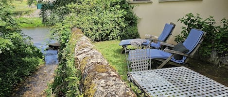 Un muro de piedra con una mesa de metal y dos sillones reclinables a rayas azules.