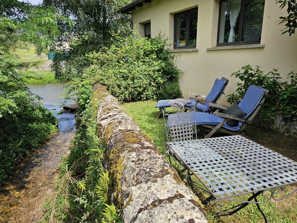 A stone retaining wall with a metal table and two blue-striped lounge chairs.