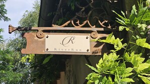 Un letrero metálico rústico con la inscripción 'RiverRun' fijado a un edificio.