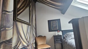 Un dormitorio con una cama grande, una silla, una mesita y un cuadro en la pared.