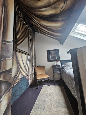 Un dormitorio con una cama grande, una silla, una mesita y un cuadro en la pared.