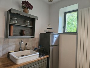 Una cocina con un refrigerador de acero inoxidable, un lavamanos blanco y una repisa con frascos y un florero.