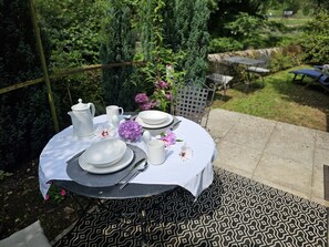A round table set outdoors with white plates, a pitcher, and a vase of flowers.