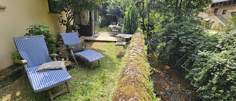 Un jardin avec deux chaises longues, une petite table et un mur en pierre.