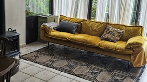 Una habitación con un sofá amarillo mostaza, un tapete estampado y vistas a la vegetación a través de cortinas translúcidas.