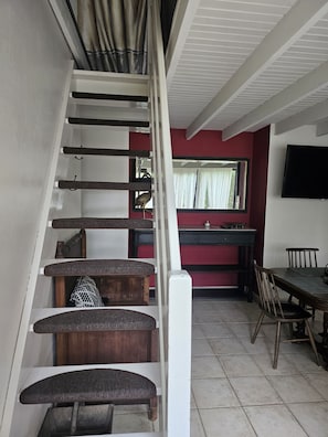 Una escalera conduce a un comedor con una pared roja y un televisor montado sobre la mesa.