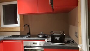 Une cuisine de taille réduite avec des placards rouges, un grille-pain noir et une cuisinière.