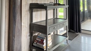 A room with a wooden wall, a mirror, a console table with books, and a view through a glass door.