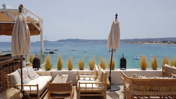 A wooden deck with wicker furniture and umbrellas overlooking a calm sea with boats.