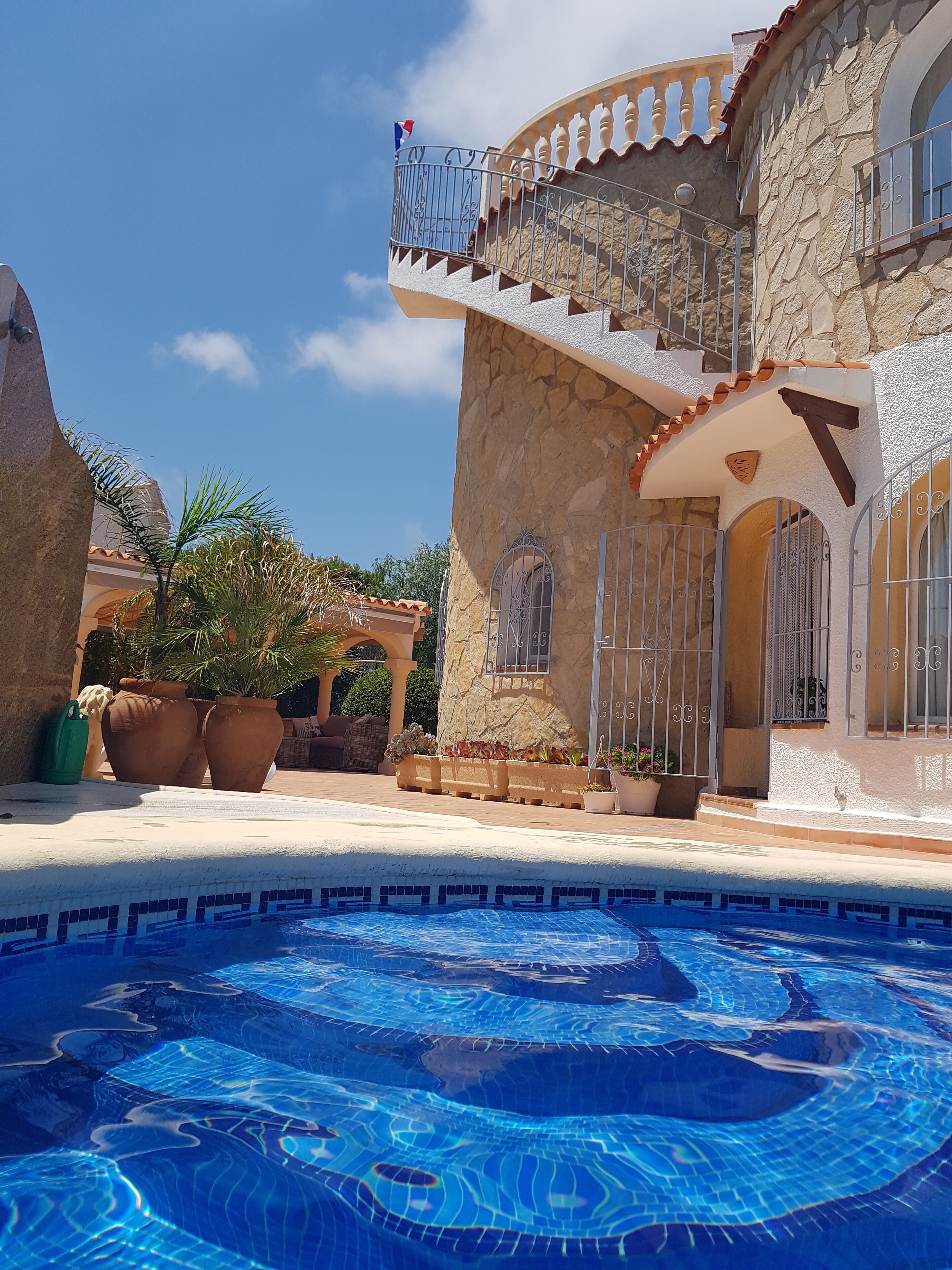 A pool area with a stone building, a balcony with a flag, and potted plants.