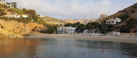 A coastal area with buildings on a hillside, a beach, and calm water.