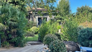A wooden deck with a garden leading to a house with a tiled roof. - Villa 6 people swimming pool port vecchio (Porto vecchio)