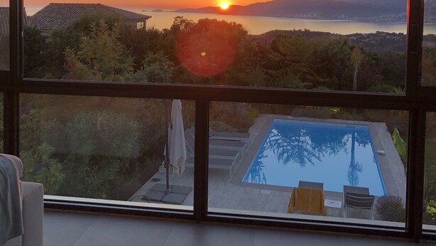 Habitación con un amplio ventanal que da a una piscina y una vista al atardecer.