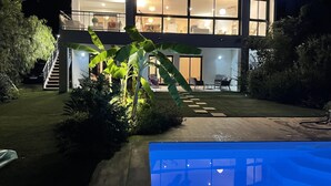 Una casa moderna de dos pisos con piscina, un jardín bien cuidado y una escalera que lleva al piso superior.