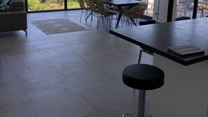 Una cocina moderna con una isla grande, comedor con sillas de mimbre y ventanas amplias que ofrecen vista al mar y las montañas.