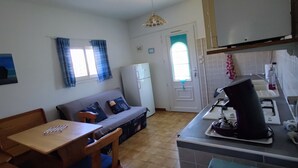 A compact kitchen with a dining area, a refrigerator, and a window with curtains. - Small cozy nest for peaceful vacations (Lucciana)
