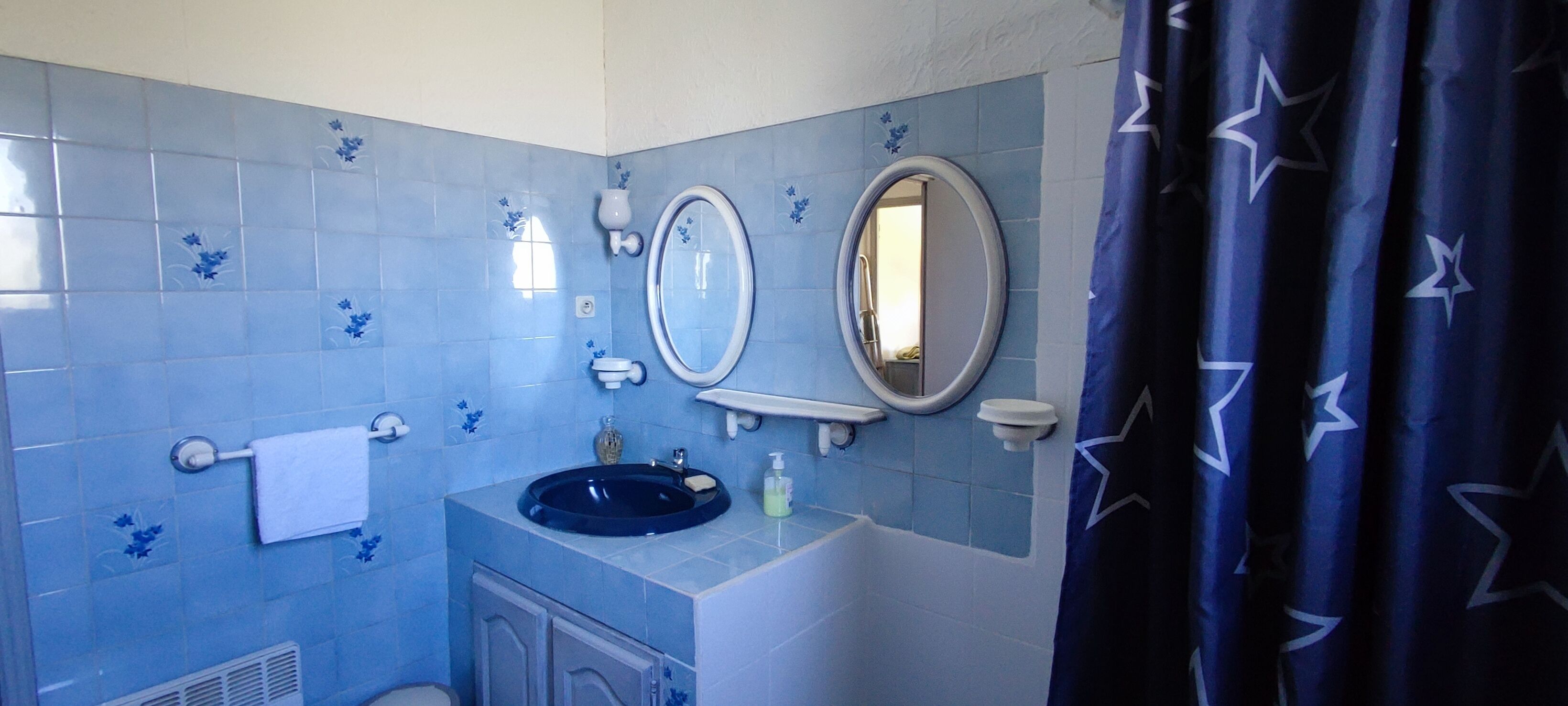 Ein Badezimmer mit blauen Fliesen, einem Waschbecken, einem Spiegel und einer Duschvorhang.